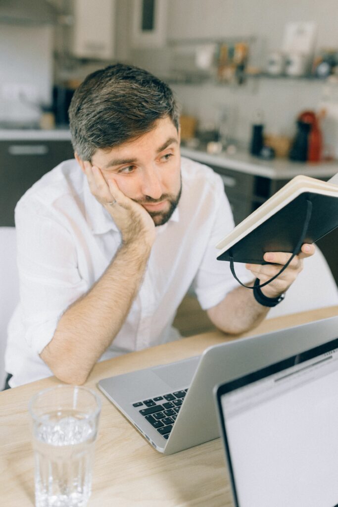 Chef d'entreprise pensif devant son ordinateur portable tenant un carnet de notes lors d'une session d'organisation
