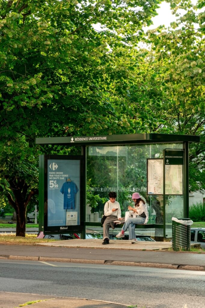Deux lycéens assis sur un banc d'arrêt de bus, absorbés par leurs smartphones, illustrant la gestion du temps numérique.