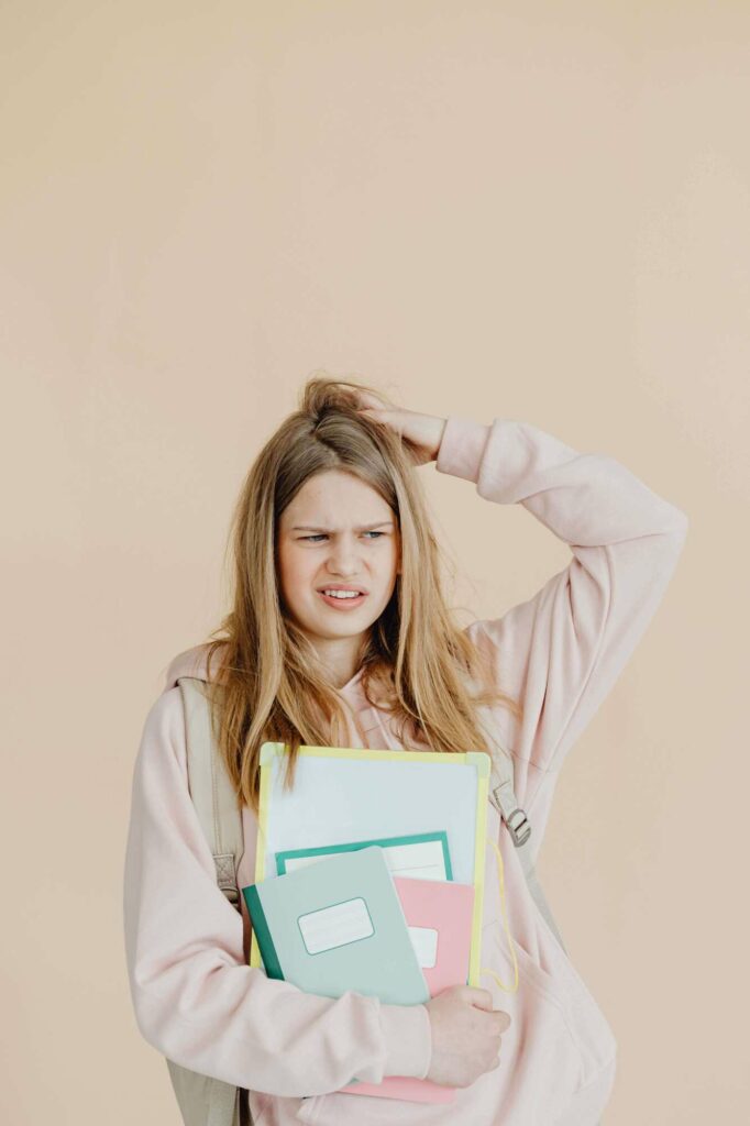 Jeune étudiante confuse et dubitative tenant des cahiers de cours contre elle.
